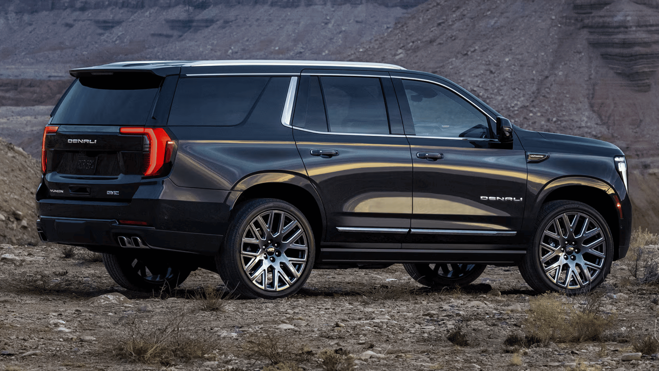 2025 GMC Yukon Denali in black, parked against a rocky desert backdrop, showcasing luxury and size near NC.