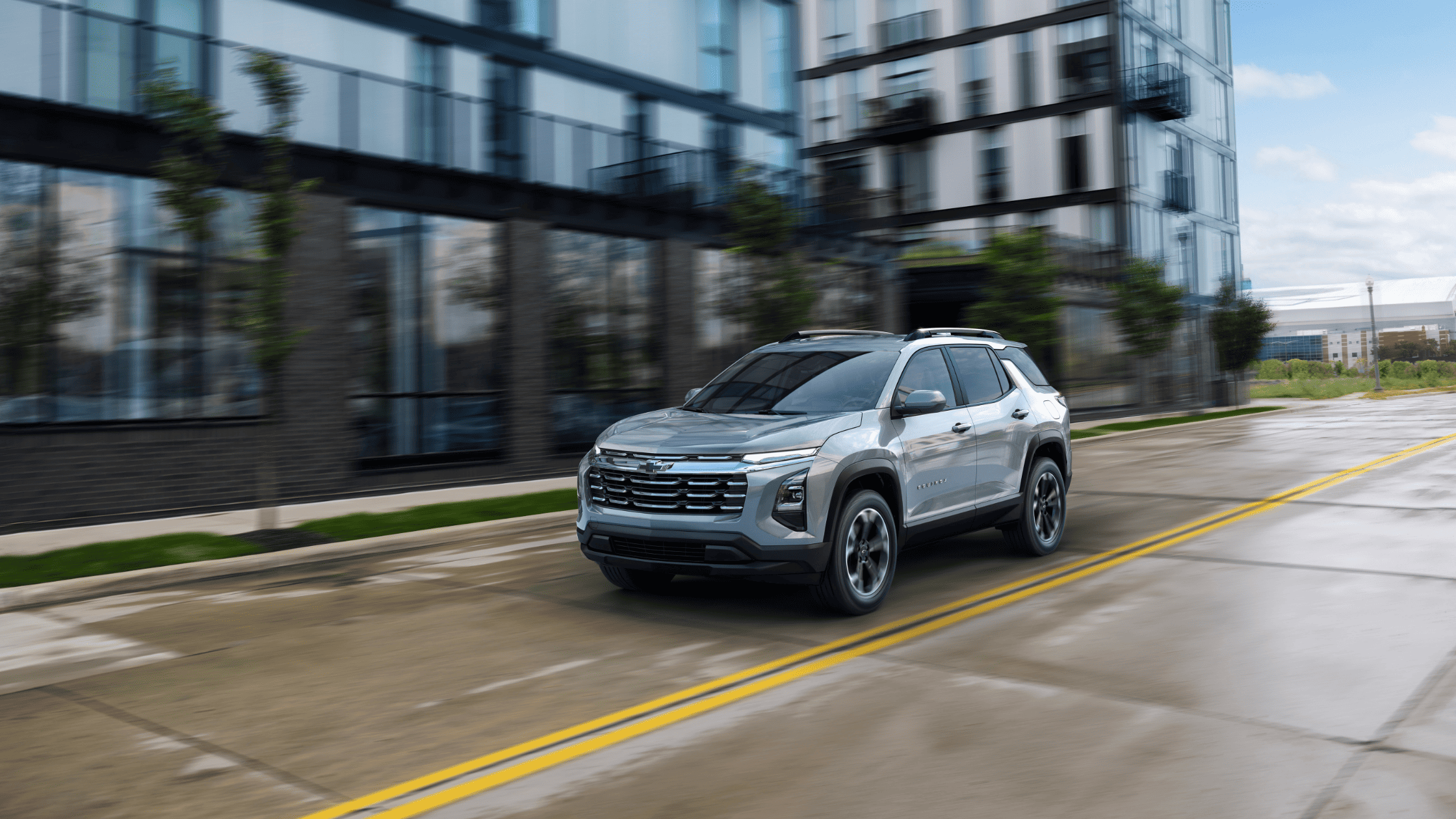 2025 Chevrolet Equinox driving past urban buildings in West Jefferson, NC, spotlighting its modern SUV design and smart tech.