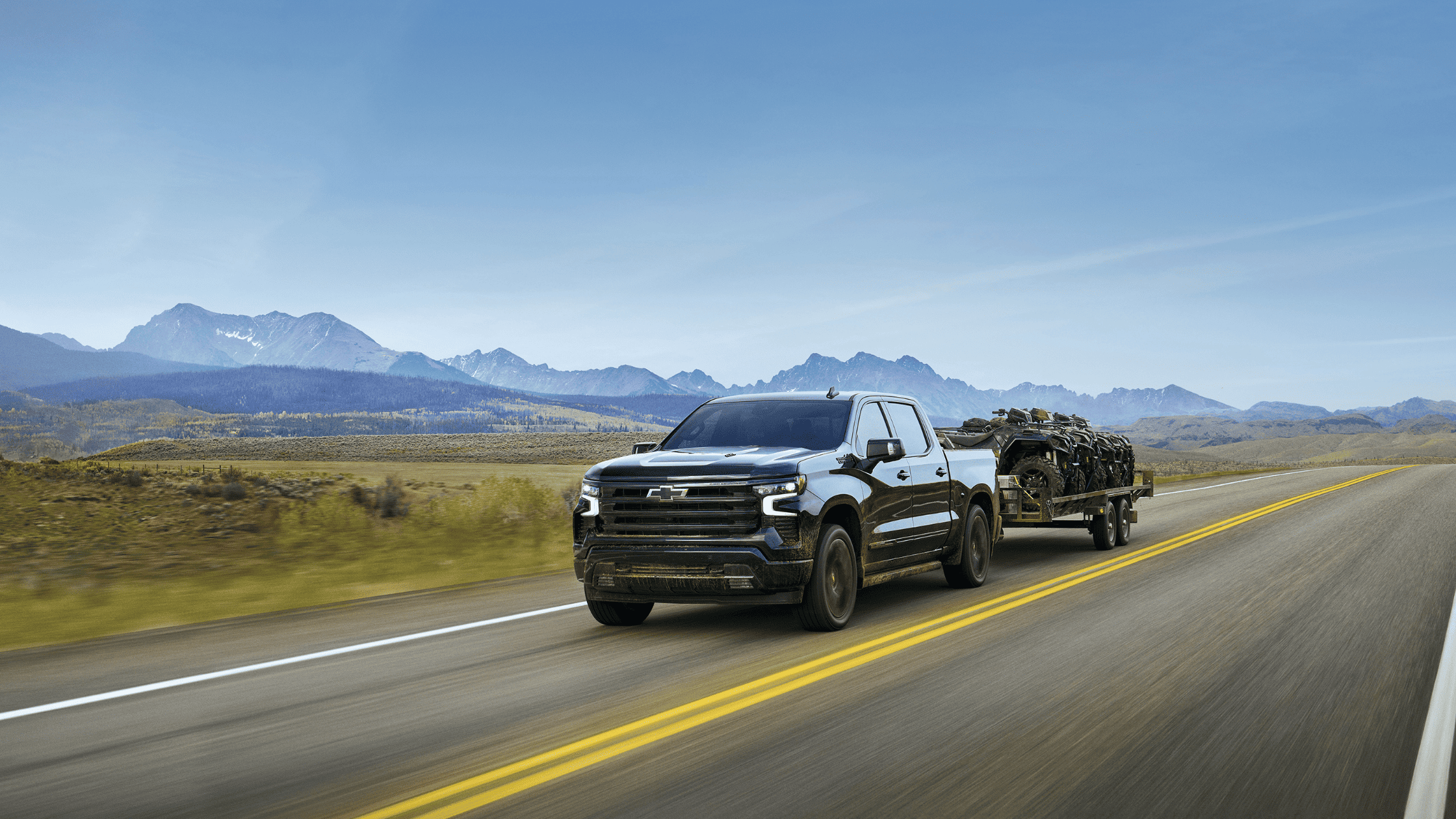 2025 Chevrolet Silverado towing ATVs along a scenic highway near West Jefferson, NC, built for power, reliability, and outdoor capability.