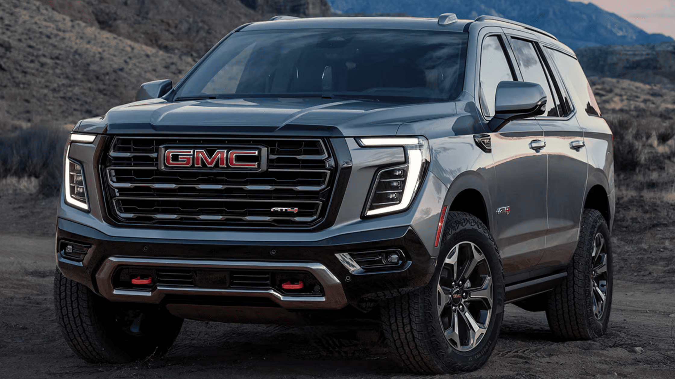 Front view of the 2025 GMC Yukon XL AT4 on rocky terrain near West Jefferson, NC, showing its bold grille and LED lights.