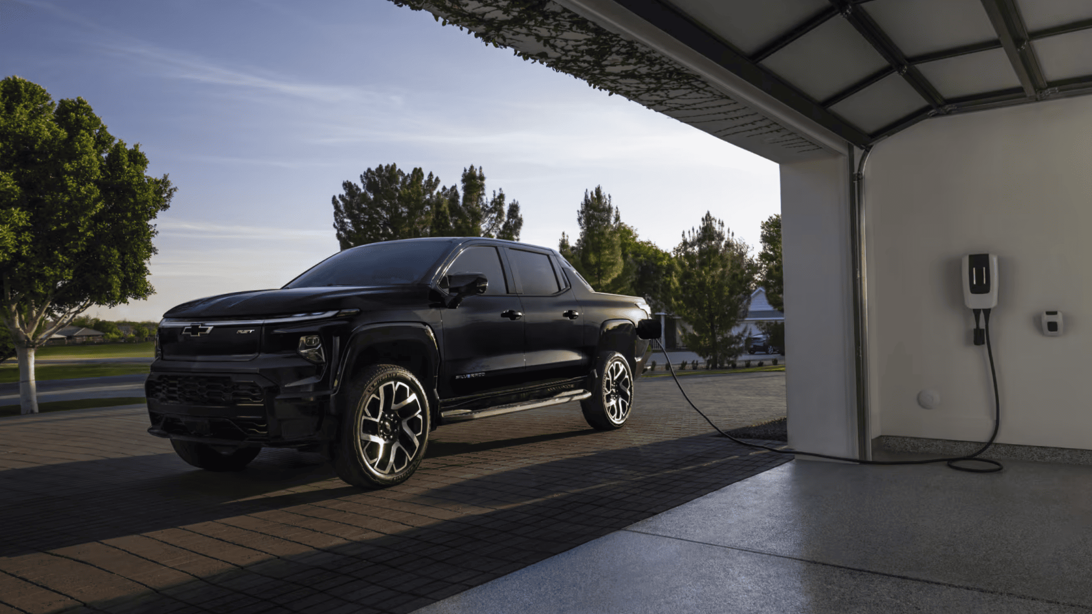2025 Chevrolet Silverado EV parked in a driveway, plugged into a home charging station in West Jefferson, NC.