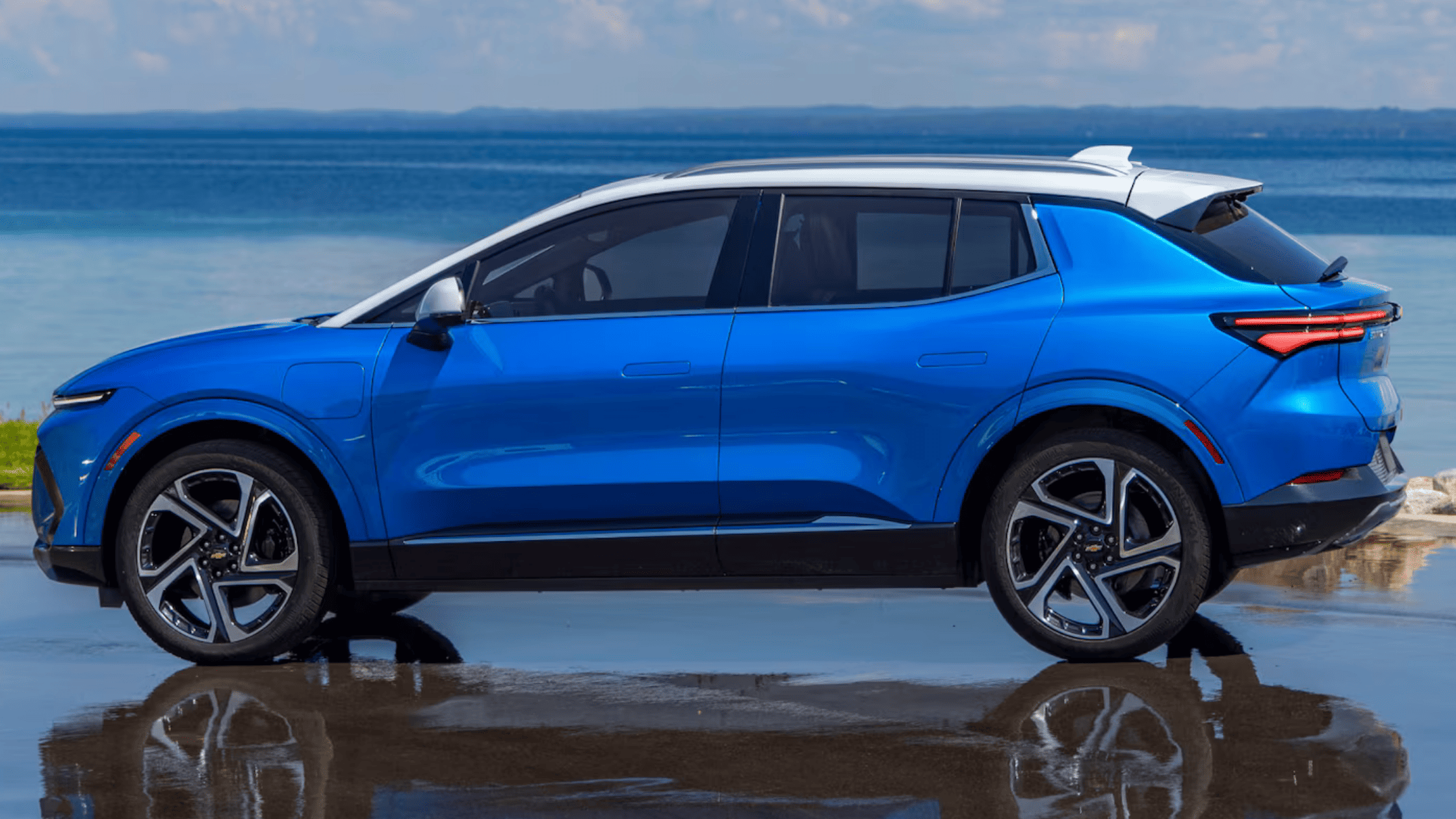 Side profile of a blue 2025 Chevrolet Equinox EV reflecting on wet pavement by the waterfront near West Jefferson, NC.