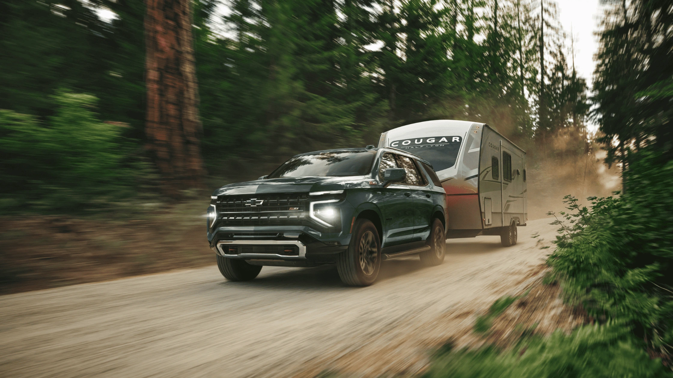 2025 Chevrolet Tahoe towing a camper trailer through a forested dirt road near Morganton.