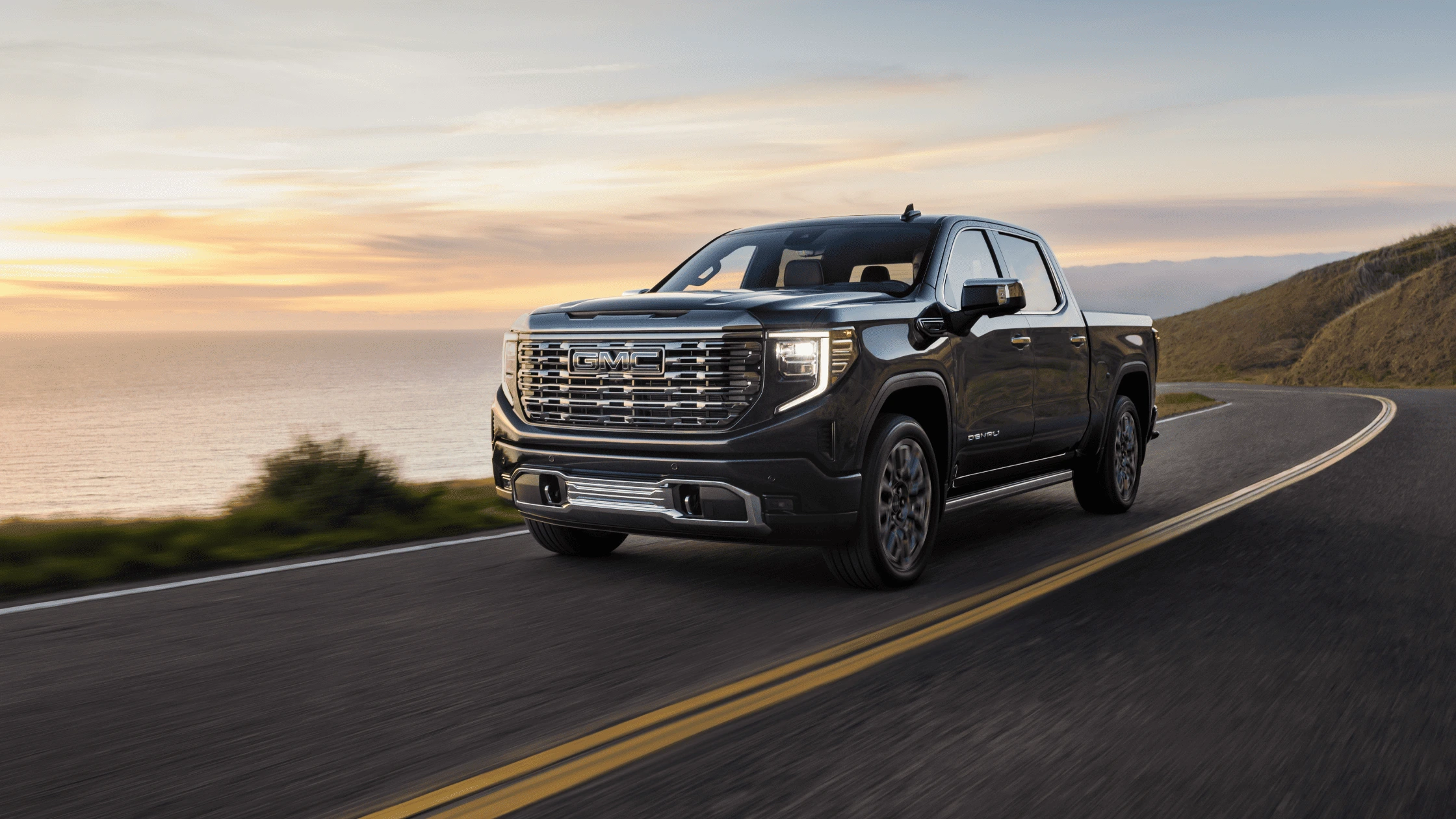 2025 GMC Sierra 1500 driving along a coastal mountain road at sunset near Morganton.