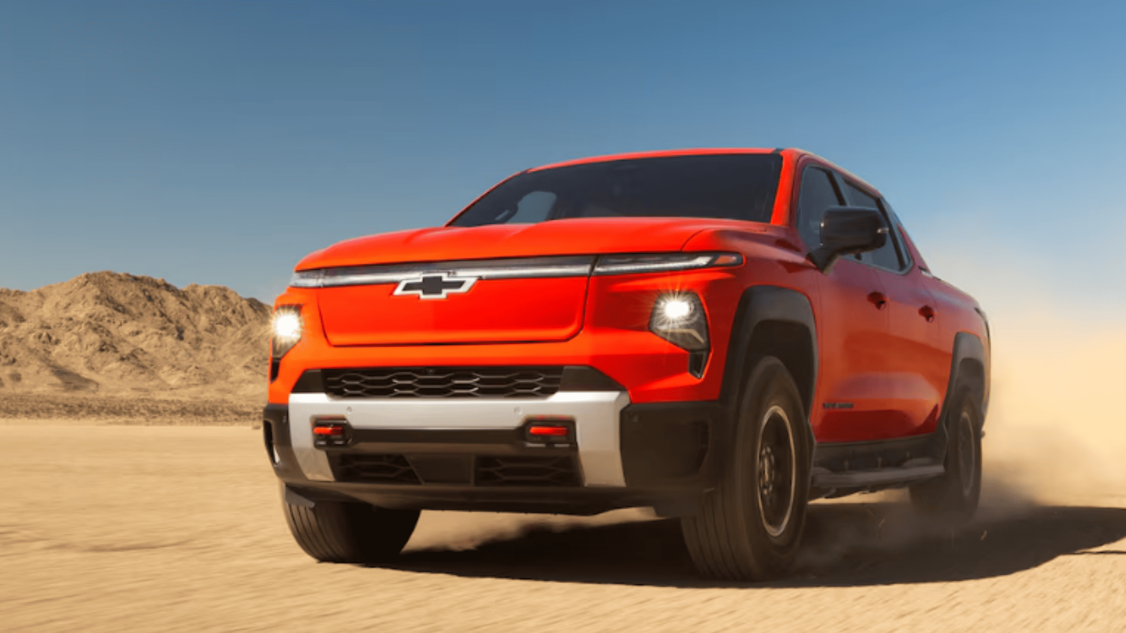 2026 Chevrolet Silverado EV driving on desert terrain, highlighting bold electric pickup design, LED lighting, and off-road-ready stance.