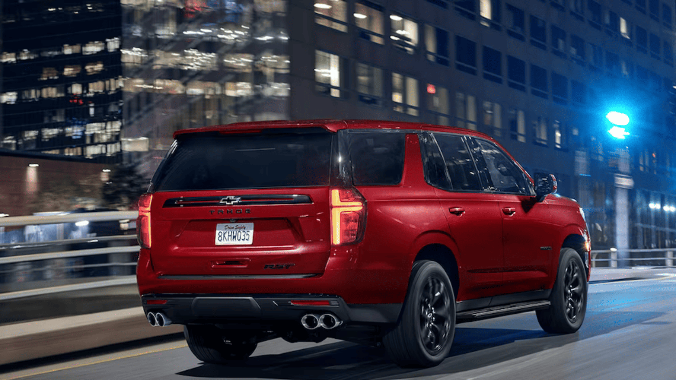 Rear view of red Chevrolet Tahoe RST driving through a city at night.