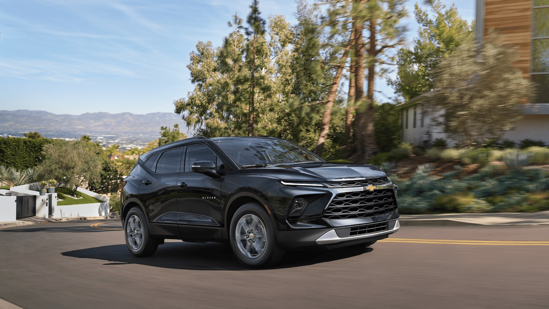 Black Chevrolet Blazer driving through a neighborhood with trees and hills.