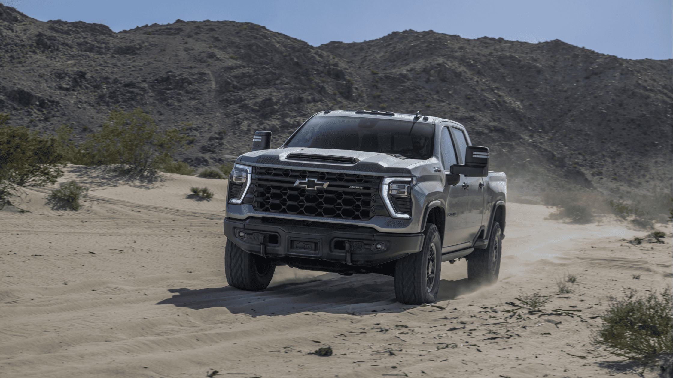 Chevrolet Silverado ZR2 charging through desert sand with dust trailing behind.
