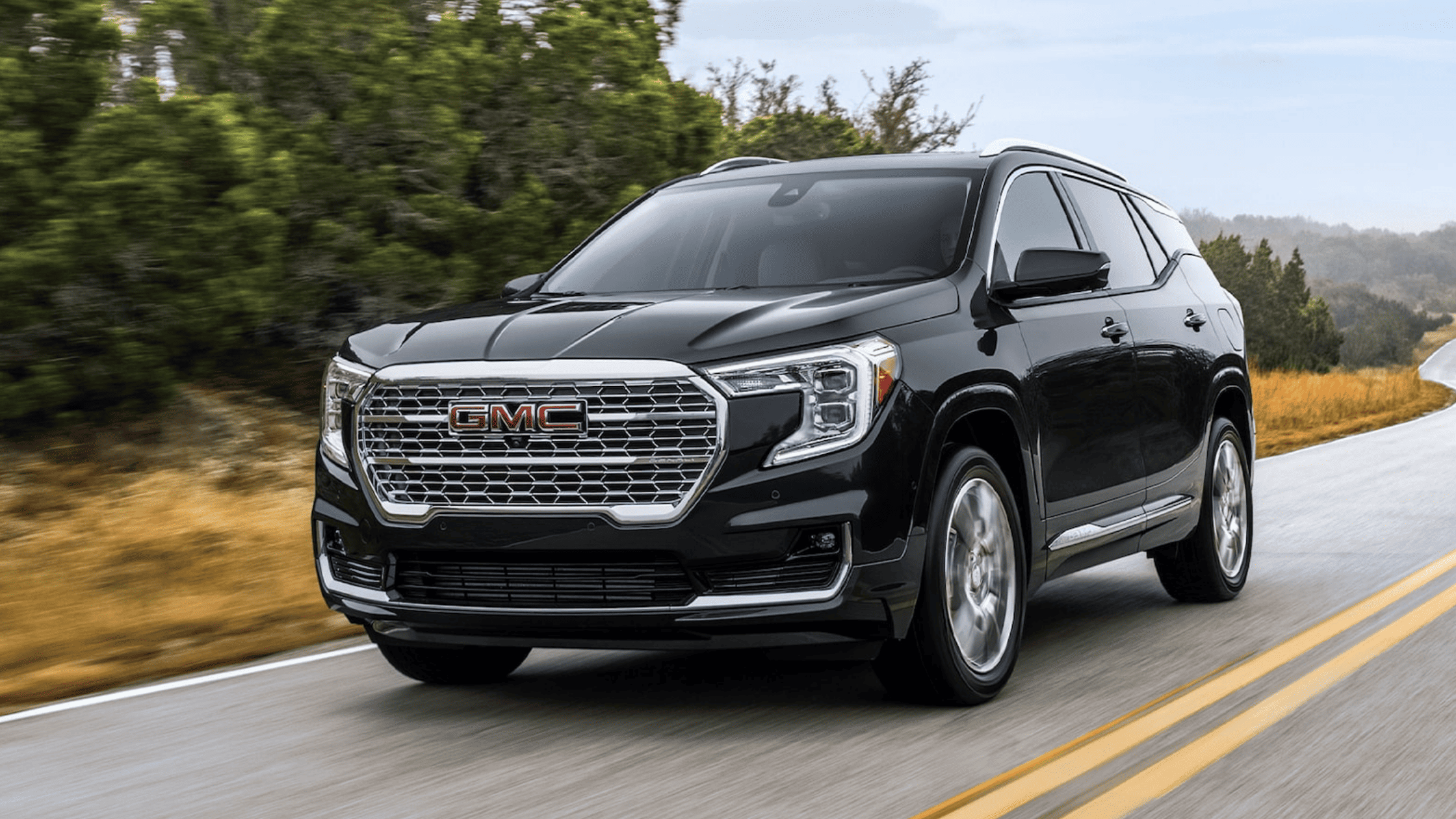 Front view of black GMC Terrain Denali driving on a winding road through the woods.