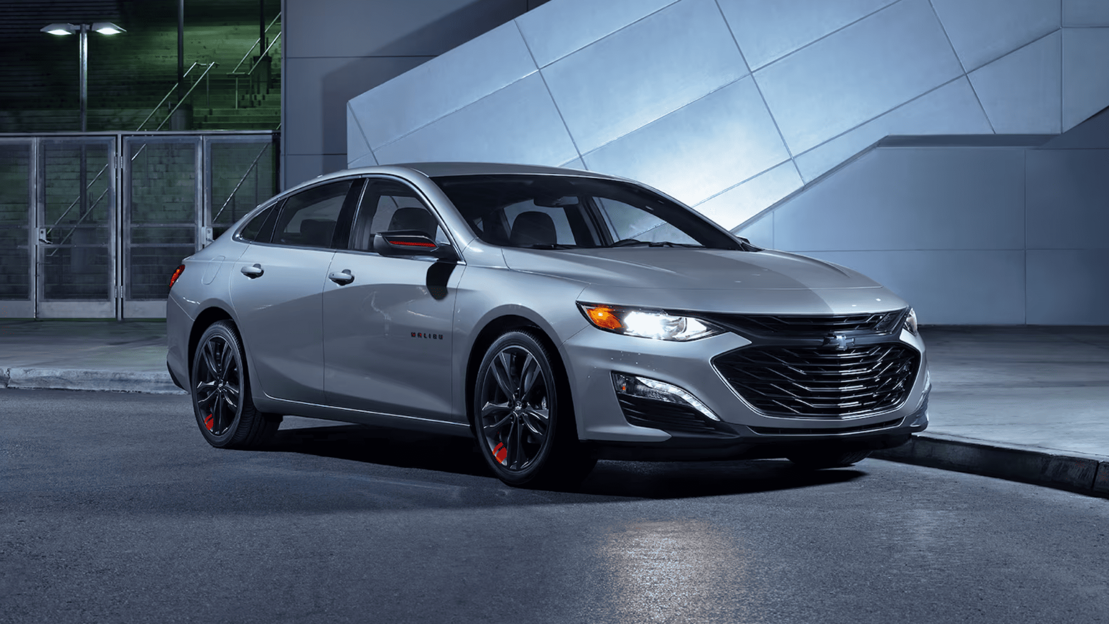 2025 Chevrolet Malibu parked at night with headlights on and sleek silver exterior