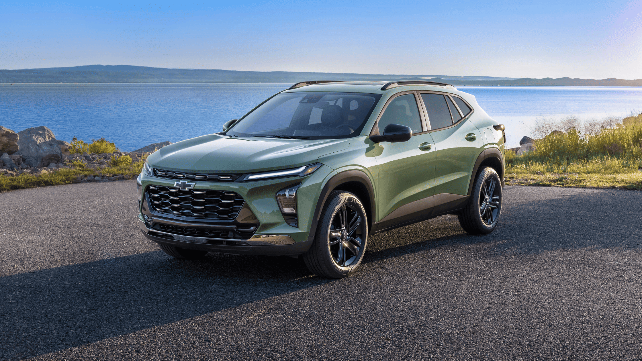 Front-side view of a green Chevrolet Trax parked by a lake with blue skies