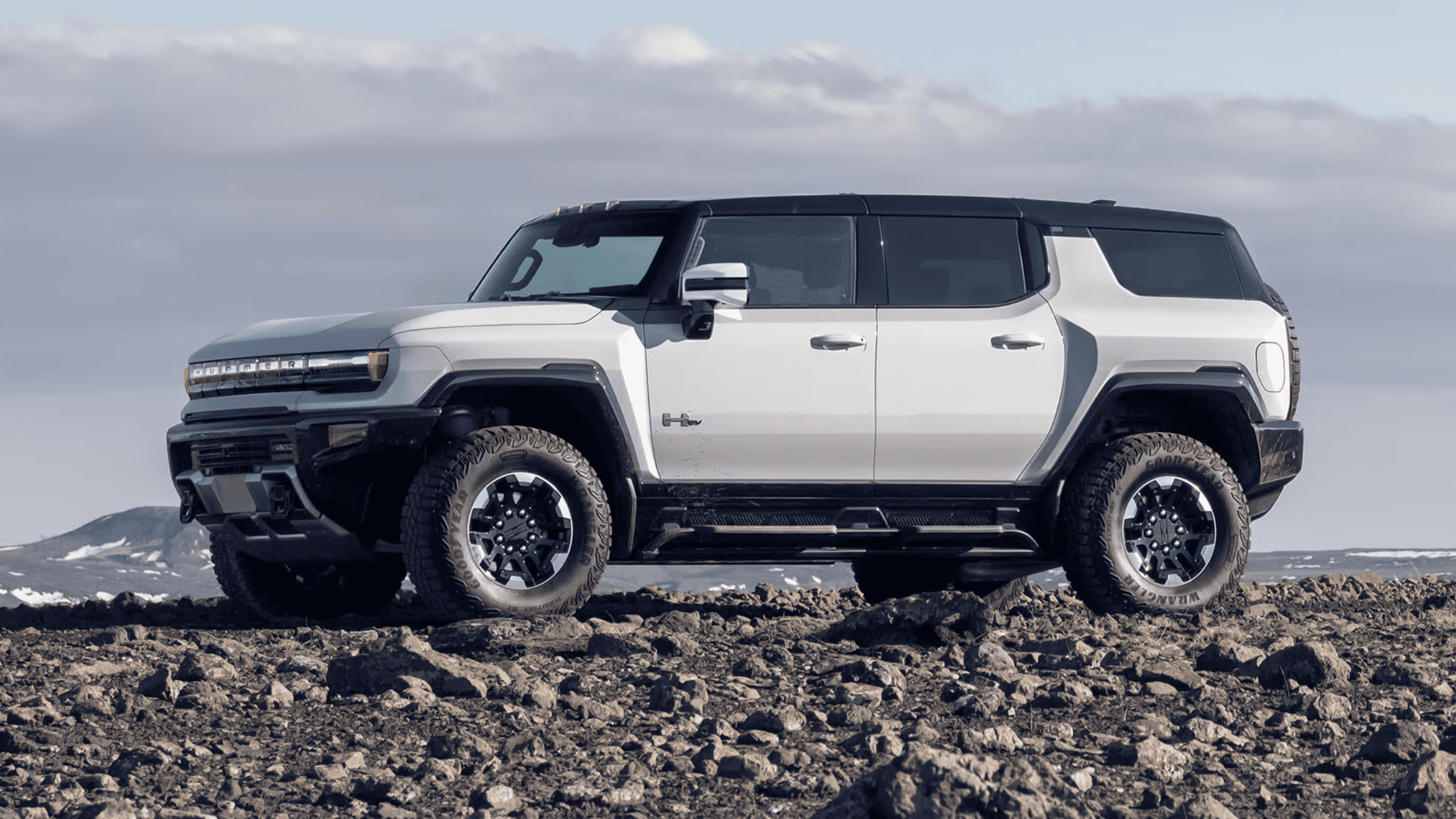 2025 GMC Hummer EV SUV parked on rocky terrain with a mountain backdrop