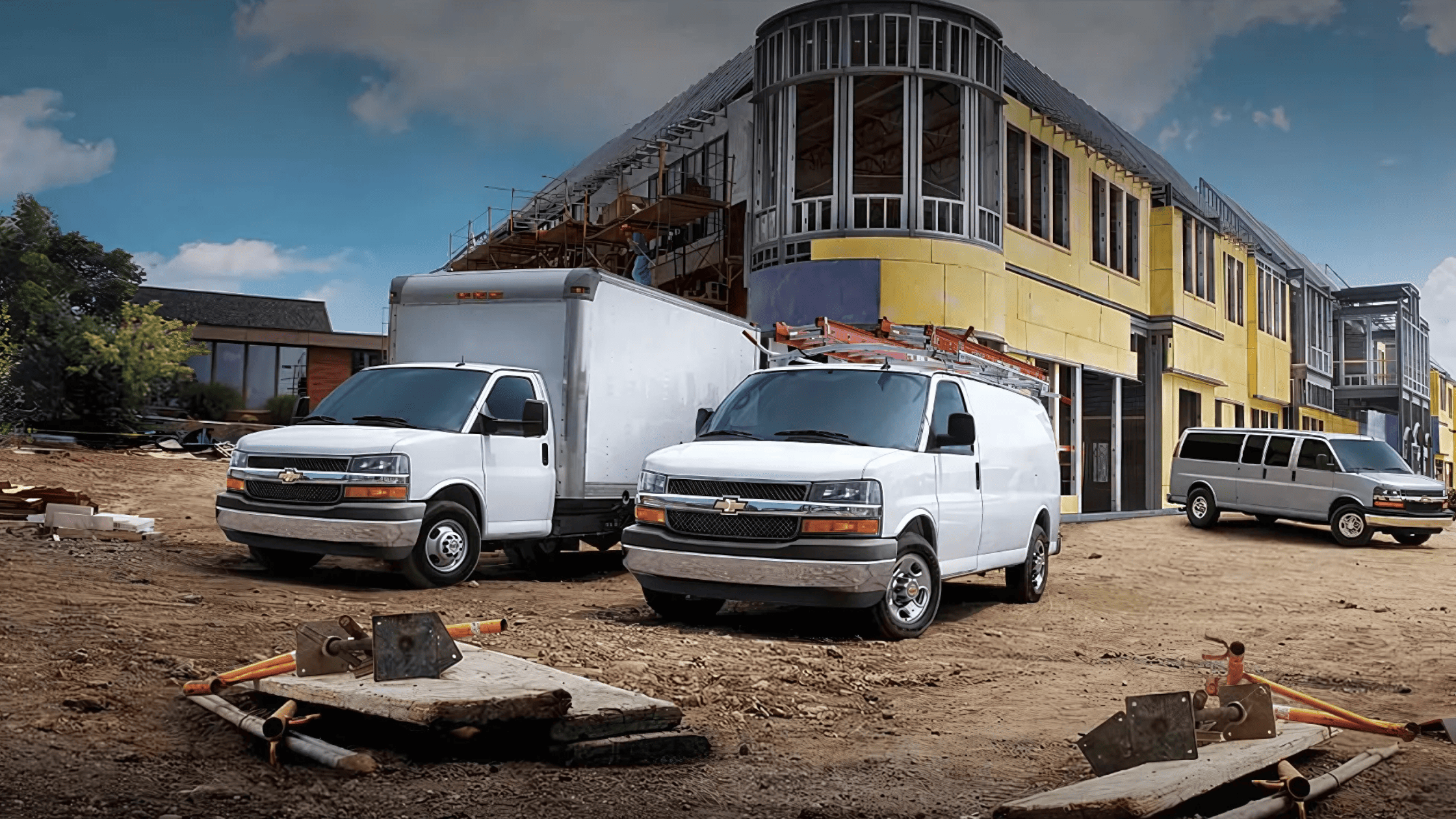 Three Chevrolet Express vans at a construction site with unfinished buildings in background