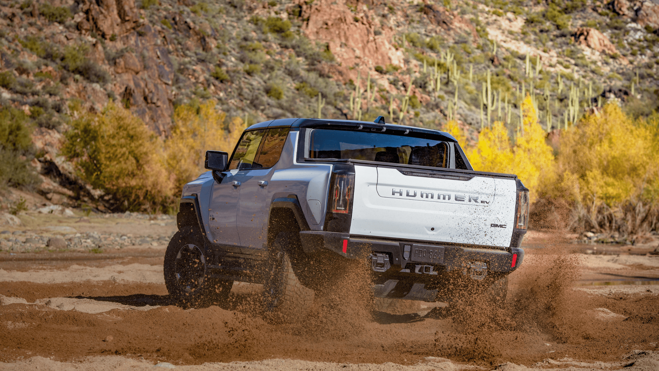2024 Hummer EV kicking up dirt while driving off-road in the desert.