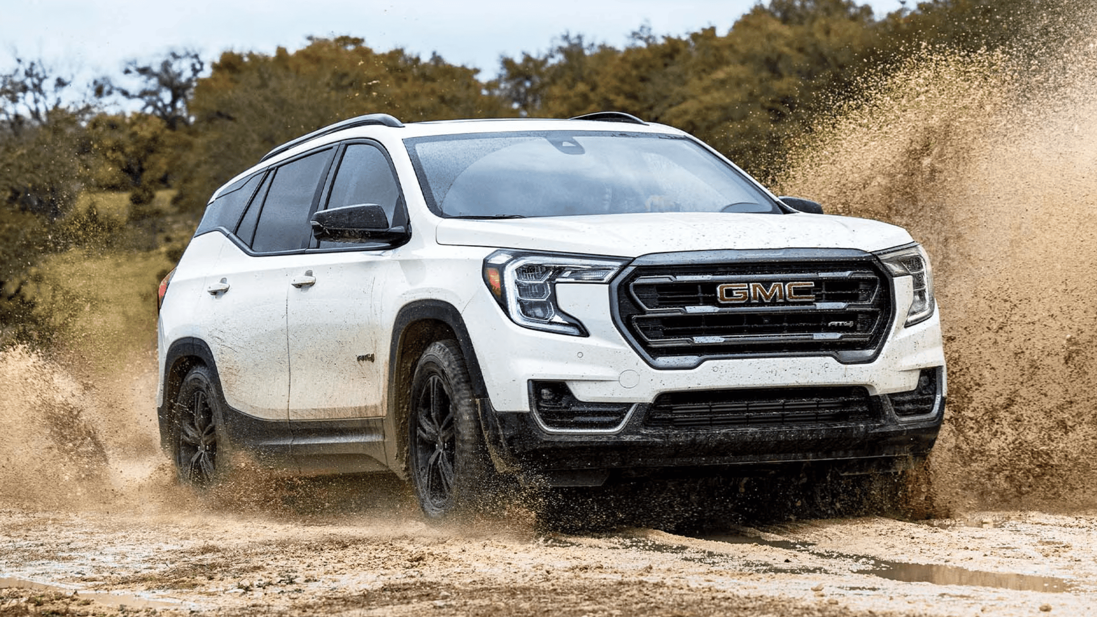 2024 GMC Terrain driving through mud with splash effect in off-road setting
