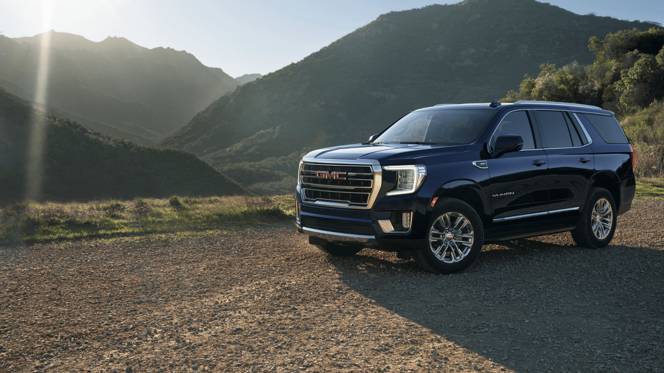 2024 GMC Yukon parked on a gravel road with mountains in the background.