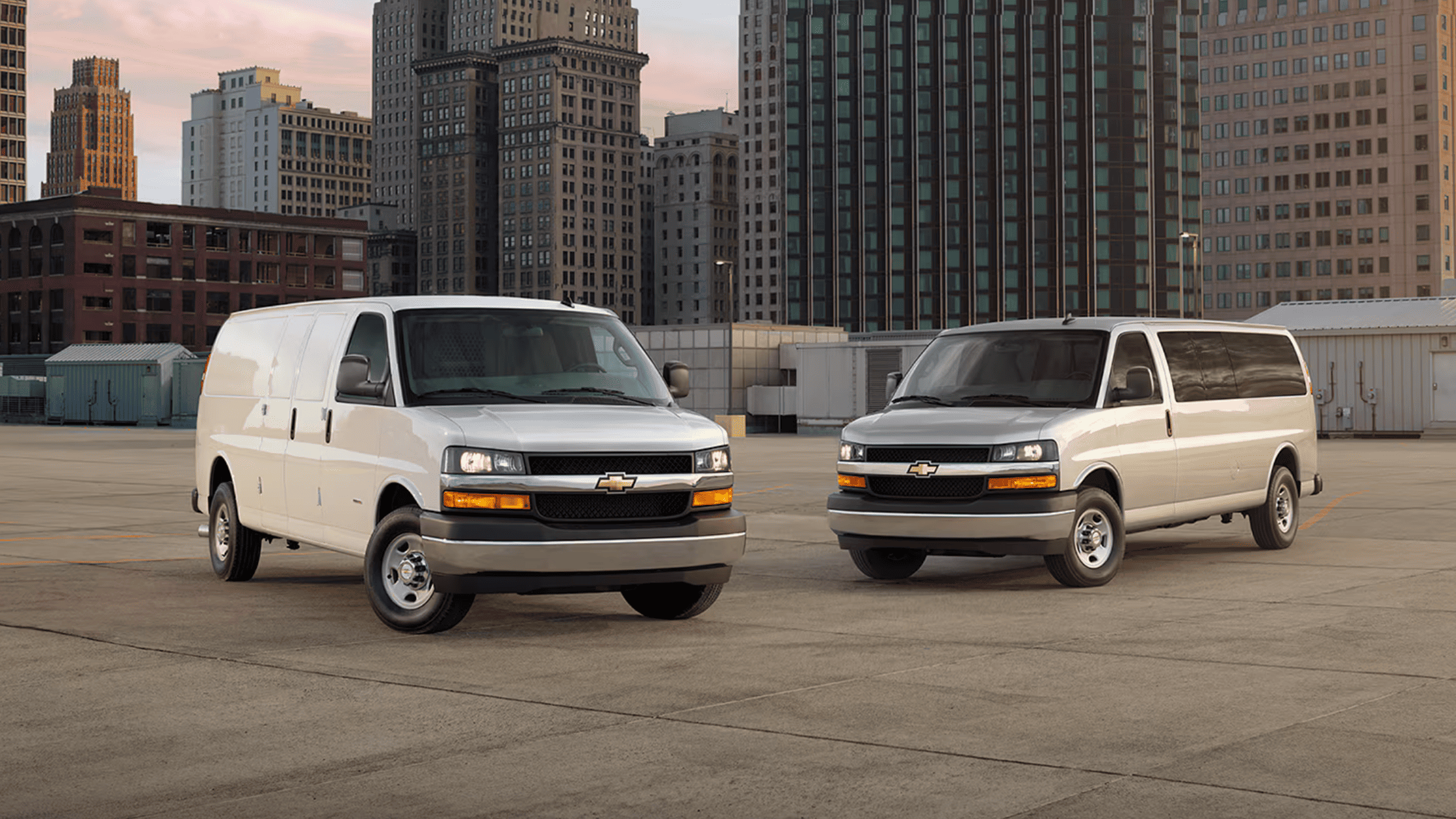 Two Chevrolet Express vans parked in a city rooftop lot