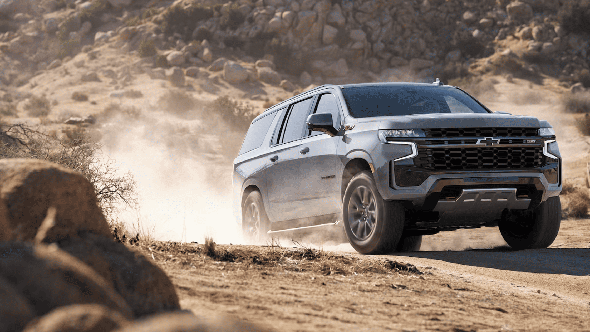 2024 Chevrolet Suburban driving off-road in dusty desert terrain.