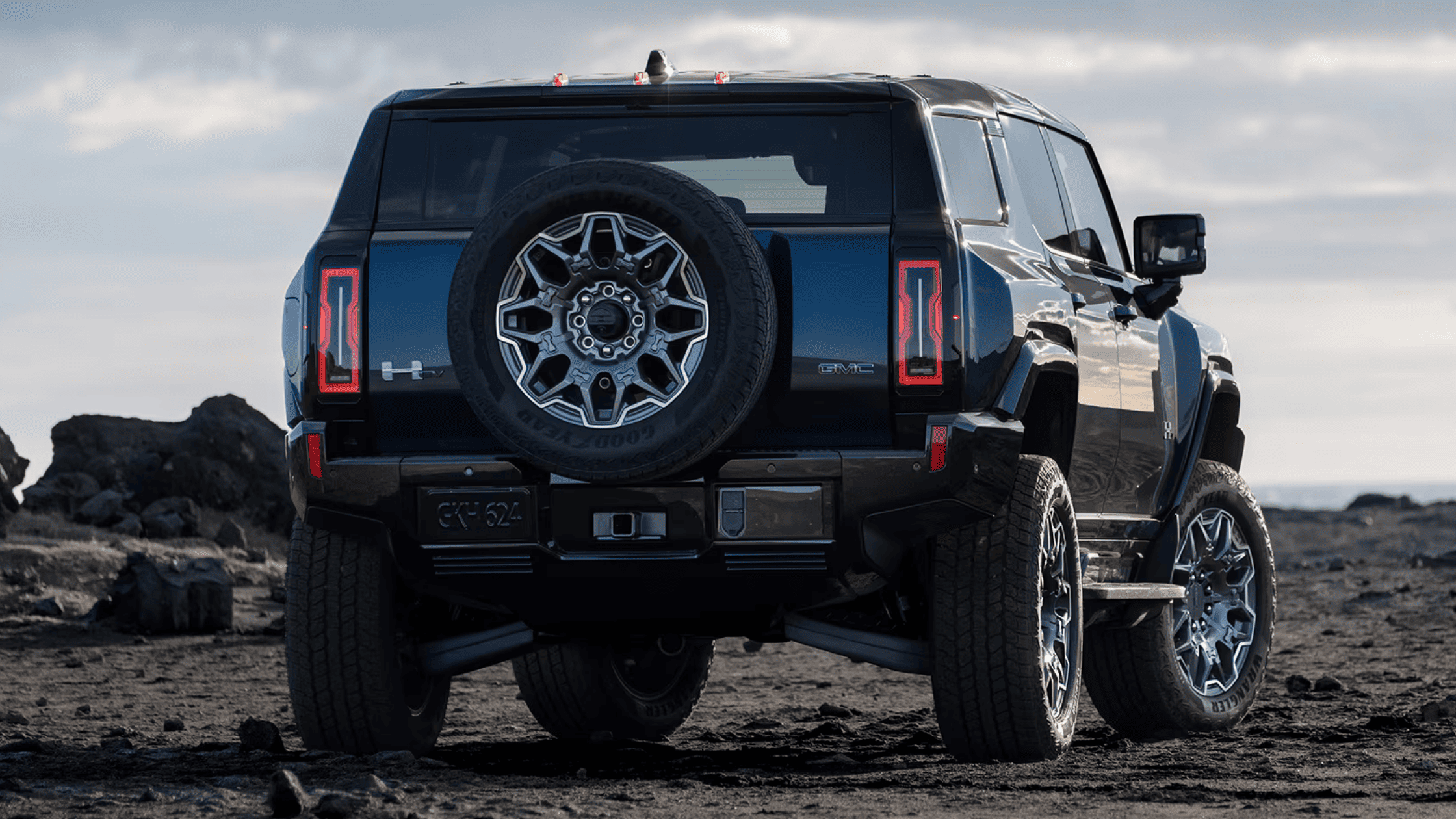 Rear view of 2025 GMC Hummer EV SUV with spare tire and off-road wheels on rugged terrain