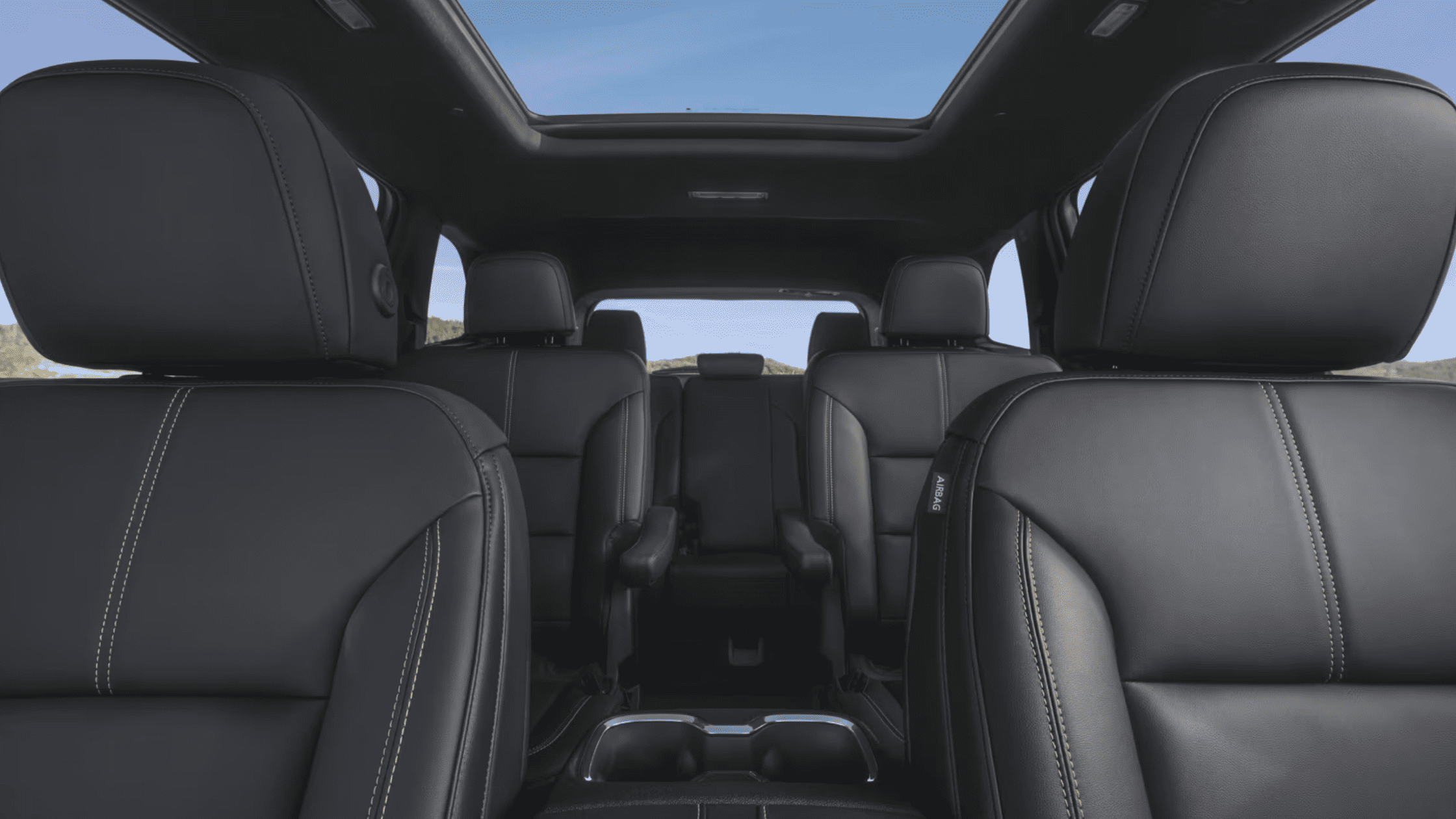 Interior view of the 2025 GMC Acadia showcasing black leather seats and panoramic sunroof with three-row seating layout.