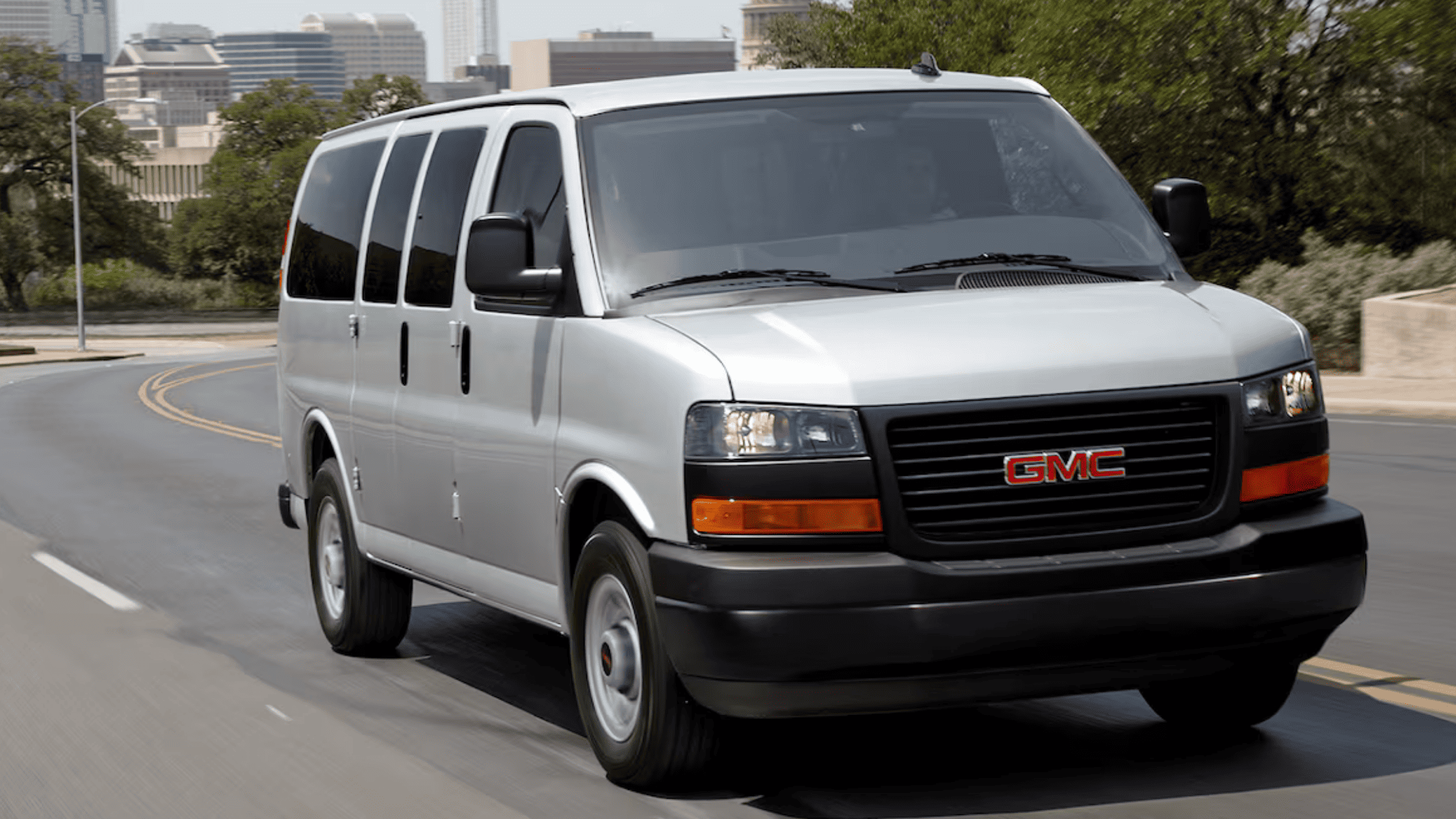 Silver 2025 GMC Savana Passenger Van driving through city streets near West Jefferson, NC, ideal for large families or commercial fleets.