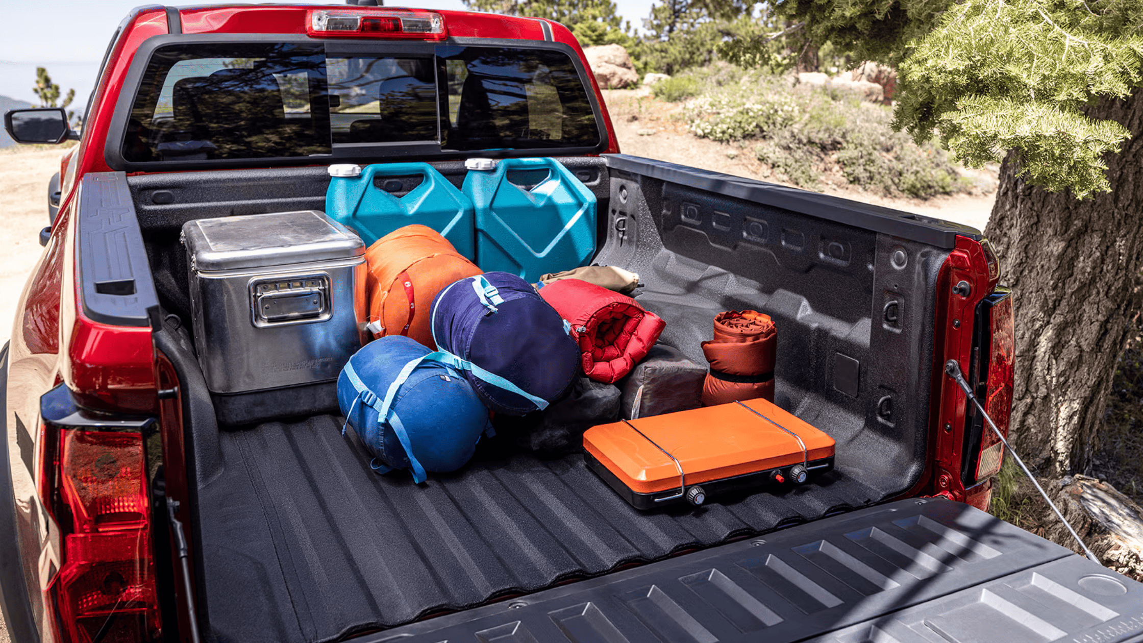 Chevy Colorado bed filled with camping gear in wooded area
