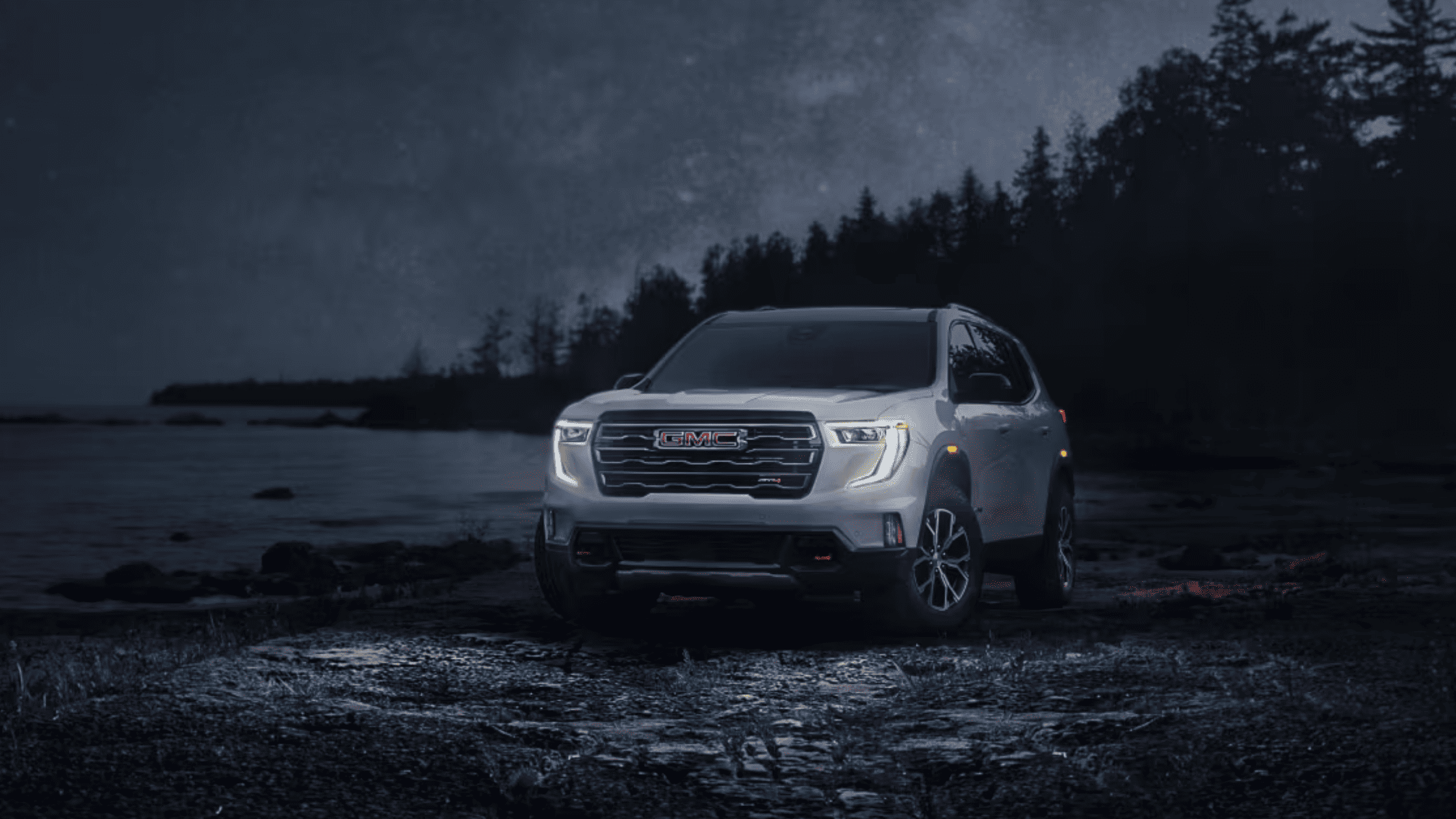 2025 GMC Acadia driving at night by a lakeside under starry sky