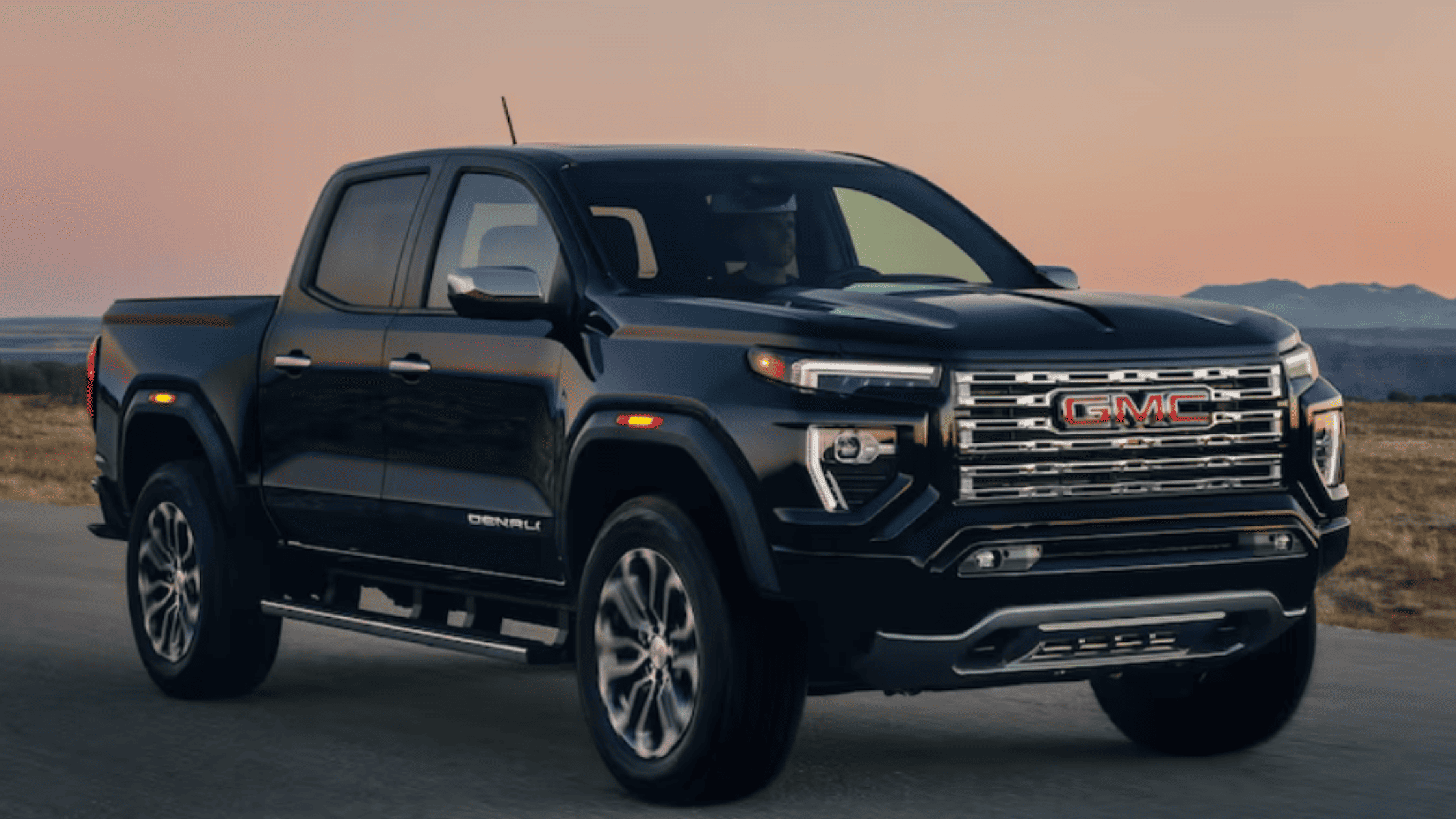 2026 GMC Canyon near Morganton, NC, captured on an open highway at sunset, emphasizing its bold Denali front grille and performance appeal.