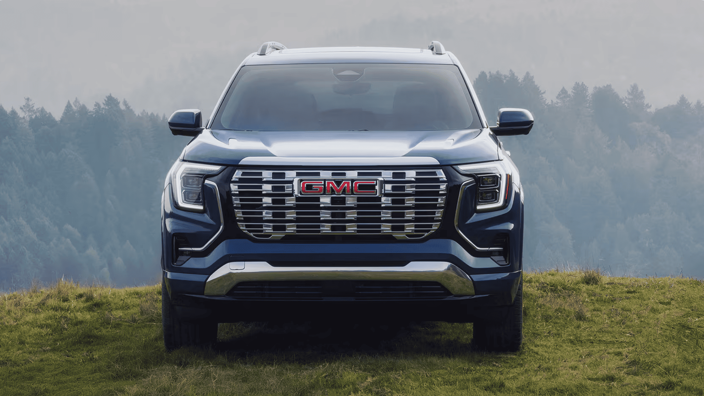 Front view of a 2026 GMC Terrain SUV parked on grassy terrain in Boone, NC, showcasing bold grille design and rugged styling.